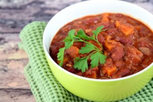 Vegetable chili in a green bowl with a sprig of parsley on top